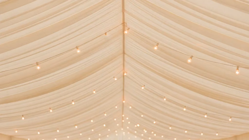 White marquee interior with swagged ceiling draping and warm fairy lights above laid tables