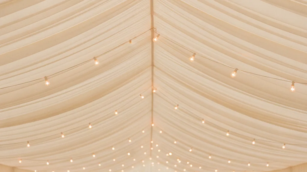 White marquee interior with swagged ceiling draping and warm fairy lights above laid tables